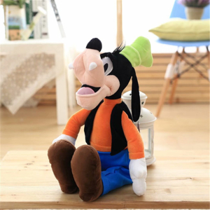 Pluche van de goofy figuur van Disney zittend op een parketvloer, hij draagt een blauwe broek en een oranje topje